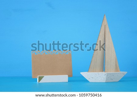 nautical concept image with sail boat and empty note over blue wooden table and background