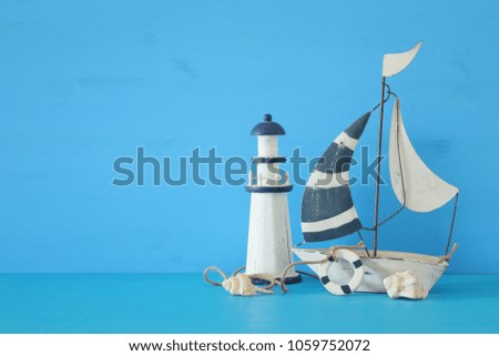 nautical concept with white decorative sail boat, lighthouse, seashells over blue wooden table and background