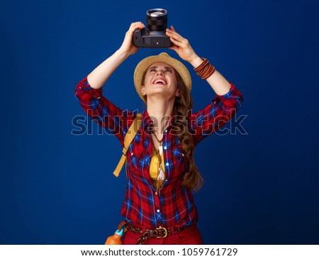 Searching for inspiring places. smiling healthy woman hiker with backpack and DSLR camera taking photo on blue background
