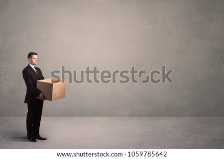 A well dressed young office worker holding an empty paper box with clear concrete wall background concept.