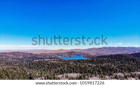 Beautiful Lake Arrowhead As Viewed From The Rim Of The World with white clouds, blue sky, green trees and purple mountains