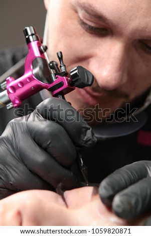 Beauty salon. Male beautician in black gloves making permanent makeup procedure on female eyebrows