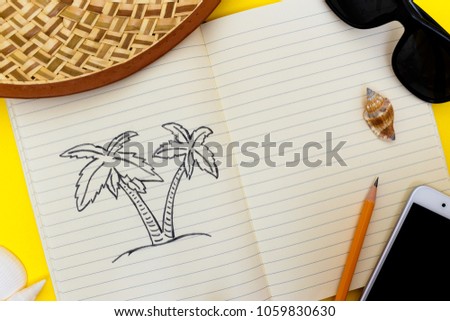 open notebook with a picture of a palm tree lies on an expressive yellow surface surrounded by various objects such as a hat, sunglasses, phone, shells.