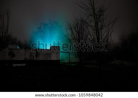 Old house with a Ghost in the forest at night or Abandoned Haunted Horror House in fog. Old mystic building in dead tree forest. Creepy house in the middle of a dark forest. Surreal lights