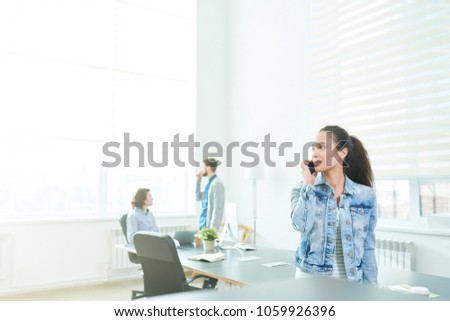 Serious ambitious attractive young Hispanic female manager in denim jacket talking on mobile phone while discussing project with client in board room