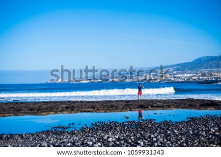 tourist see the big waves in tenerife. red pants stand up feeling the ocean. mirror on the water. taking pictures at the landscape