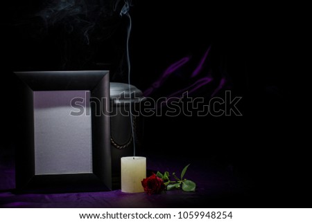 Black cemetery urn with black blank mourning frame smoky candle and  red rose on deep purple background for sympathy card