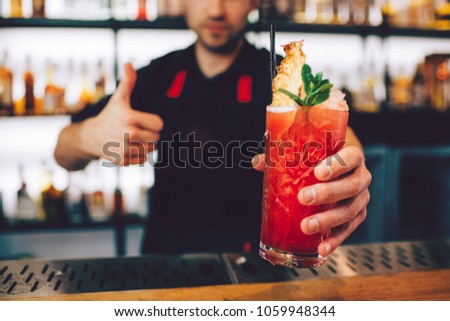 A picture of cocktail that is pepared by barman. It has nice red color. Also there is some ice on the top of the cocktail and a piece of mint with the cocktail tubule.