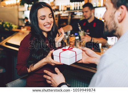 Another picture of man giving a gift to his beloved girl. She is accepting it with smile and pleasure. She is looking down to the present.