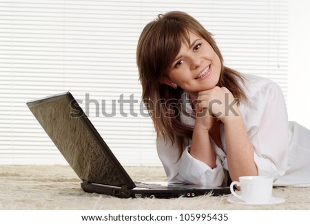 Pretty Caucasian girl lying on a carpet with a laptop