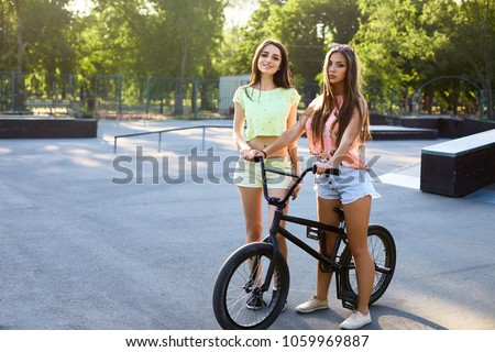 Lovely young woman with a bicycle on city background in the sunlight outdoor. Active people. Two pretty girls with bmx. Friends at skatepark.