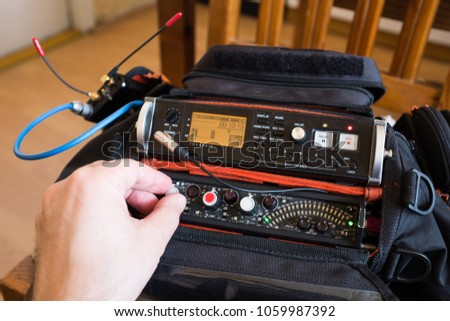 Audio engineer recording live sound on a portable sound recorder, male hand mixing sound with a rotary pot on a sound mixer, with a recorder and wireless microphone receiver set on the side