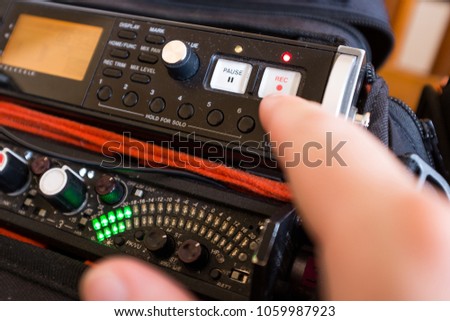 Audio engineer pushing REC record button on a portable sound recorder, with green peak meter level illuminated led bars, stereo recording