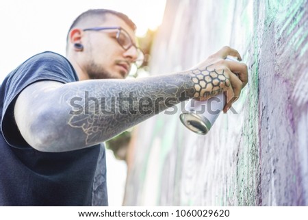 Tattooed graffiti artist painting with color aerosol on the wall - Contemporary spray write at work - Urban lifestyle,street art concept - Focus on his hand can