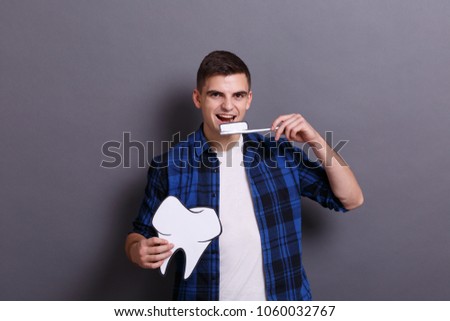 A young man holds a paper image of a tooth and a toothbrush on a gray background. Healthcare concept.