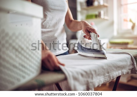 Women wearing white shirt ironing clothes on ironing board in laundry room at home Royalty-Free Stock Photo #1060037804