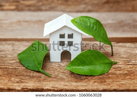Miniature white toy model house with green leaves on wooden backgdrop. Eco Village, abstract environmental background. Real estate mortgage property insurance dream home ecology concept