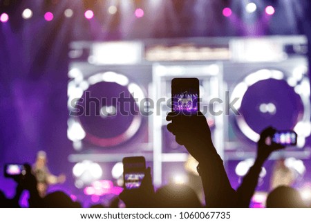 silhouette of a hand with a smartphone at a concert, record show on the stage