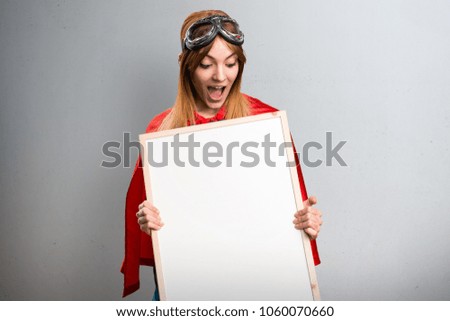 Pretty superhero girl holding an empty placard on a gray textured background