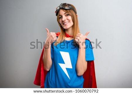 Pretty superhero girl with thumb up on a gray textured background