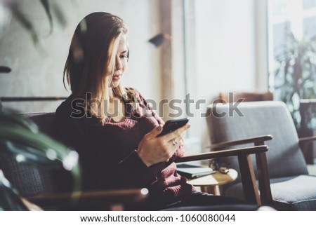 Blonde yound woman holding modern mobile phone in hands.Girl pointing fingers on empty touch mobile screen at sunny coworking place. Horizontal, blurred background