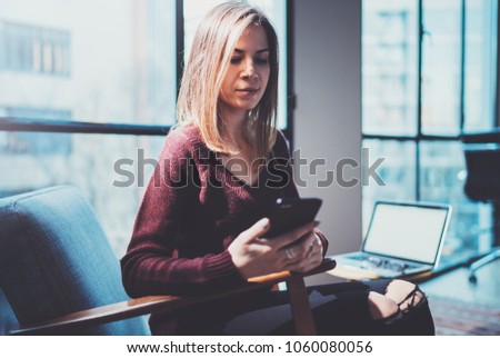 Blonde yound woman holding modern mobile phone in hands.Girl pointing fingers on empty touch mobile screen at sunny coworking place. Horizontal, blurred background