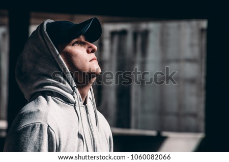 Picture that symbolizes hope. Guy in hoodie looking upwards to light. Royalty-Free Stock Photo #1060082066