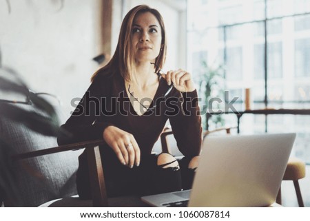 Closeup view of young beautiful woman sitting at the comfortable armchair and using laptop computer.Working process at coworking studio.Horizontal, blurred background