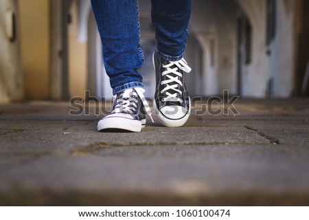 Female legs in canvas shoes walk along the cobbled street. Fashionable woman wearing sneakers walking in old town Royalty-Free Stock Photo #1060100474