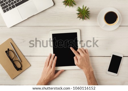 Woman's hands using digital tablet with blank screen for advertisement. Top view on female palms, laptop keyboard, coffee, phone, glasses, notebook and smartphone on wooden table background.