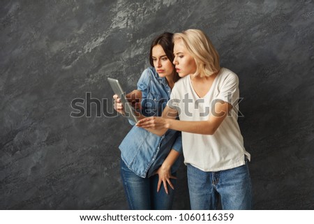 Two curious female friends with tablet at black studio background. Excited women watching interesting video or reading unexpected news online, leisure and technology concept, copy space