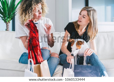Two cheerful friends discussing their purchases while curious jack russel terrier examining their shopping bags. Girls having fun at their day-off.