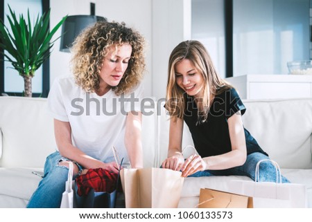 Two casual dressed girls examining each other's shopping bags with great curiosity. Girls having fun at the day-off.