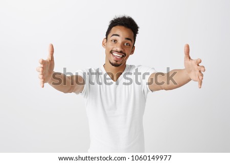 Free hugs for person who had bad day. Cheerfull kind dark-skinned male model in white t-shirt, pulling hands towards camera, wanting to cuddle, smiling broadly, welcoming friend to come into his arms Royalty-Free Stock Photo #1060149977
