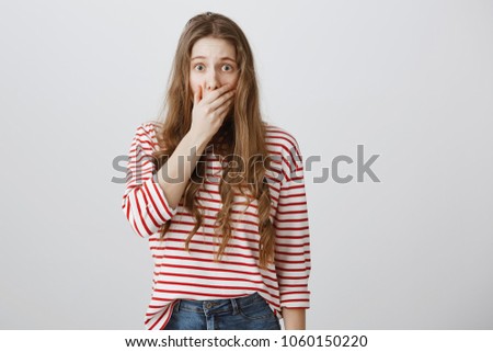 Scared and shocked girl wants to scream. Portrait of stunned fearful european woman covering mouth with palm witnessing crime or horrifying accident, staring at camera while worrying over gray wall