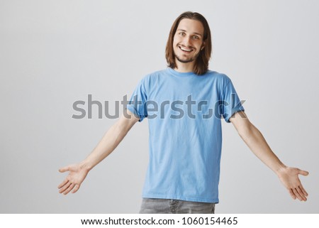 Man being sarcastic while hearing obvious things. Portrait of attractive funny caucasian male spreading hands and smiling broadly, being unaware and indifferent, standing over gray background Royalty-Free Stock Photo #1060154465