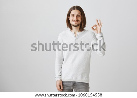 Say okay to this copy space. Relaxed friendly european man with long hair and beautiful smile raising hand, showing fine or ok gesture, expressing approval or like of idea over gray background