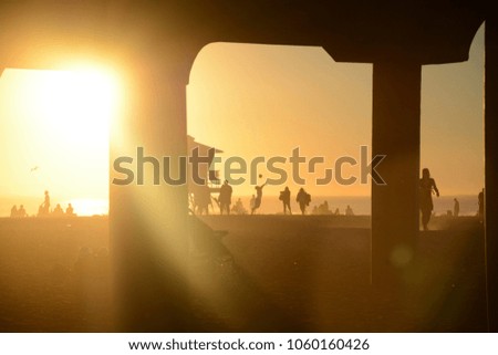 Silhouette of people playing volleyball on the beach at sunset, between the pier footings