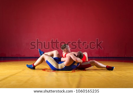 Two young man  wrestlers in red and blue uniform wrestling  on a yellow wrestling carpet in the gym. Grappling.