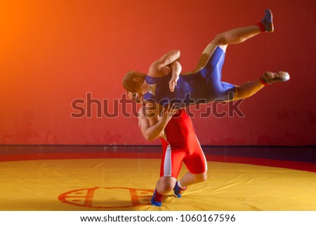 Two greco-roman  wrestlers in red and blue uniform making a   hip throw  on a yellow wrestling carpet in the gym