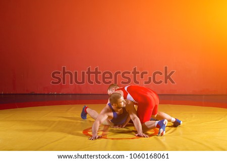 Two greco-roman  wrestlers in red and blue uniform wrestling  on a yellow wrestling carpet in the gym. Young man grappling