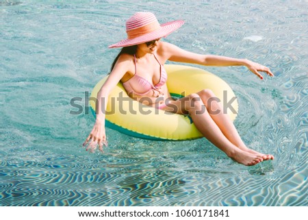 Woman wearing two piece bikini seats on rubber ring in swimming pool on summer vacation relaxing at resort spa