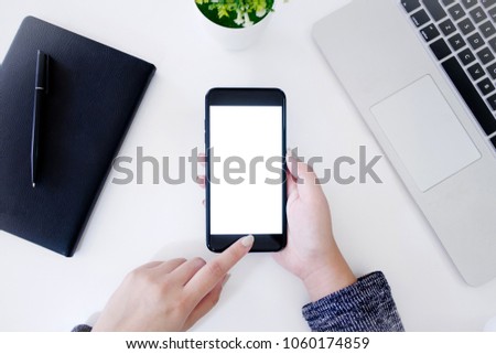 top view of hands using blank screen mobile smart phone with notebook and laptop