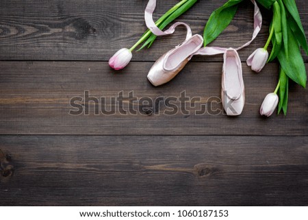 Ballet shoes near delicate flowers on dark wooden background top view copy space