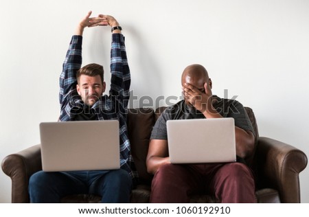 Two men using laptop sitting on sofa