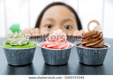 Picture of little girl is peeping tasty cupcakes on the table