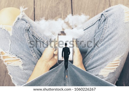 Hands holding abstract smartphone with walking businessman, road and clouds on wooden floor background. Imagination and dream concept 