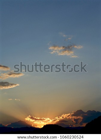 Sun setting over mountain range, dark blue sky
