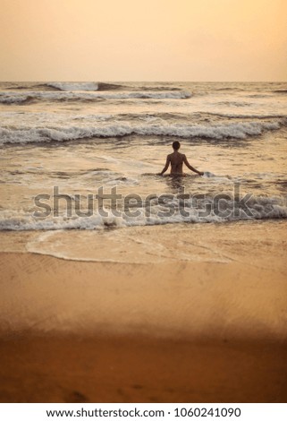 Silhouette of young woman going into the sea with small waves during golden evening light just after the sunset.