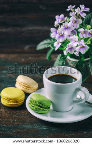 Beautiful breakfast. Morning cup of coffee with colorful macarons, on with flowers on dark background with copy space. Selective focus